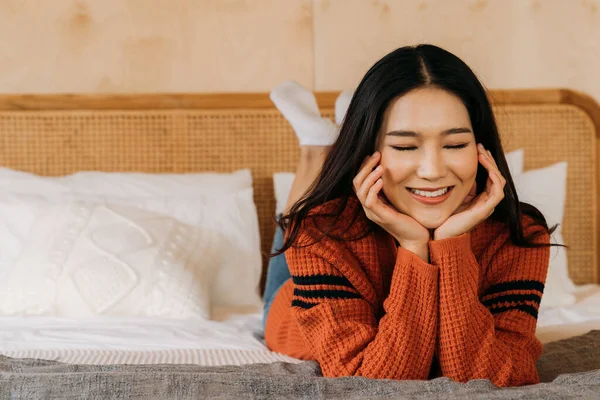 Молодая азиатка-подросток носит свитер с красивой улыбкой, глядя в камеру в спальне. Привлекательная девушка с уходом за лицом и здоровой кожей красоты Баннерное пространство. — стоковое фото