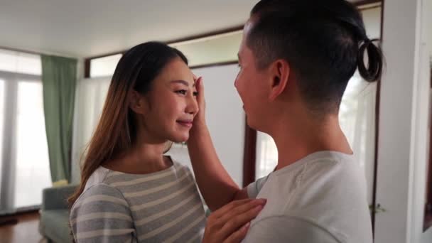 30s young adult Asian man touching cheeks of a smiling woman in the living room at home. Tender and romantic husband and wife spend family time in cozy room. — Stock Video