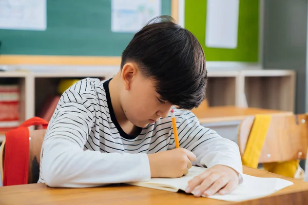 Caucasian school boy sitting in school writing in book with pencil, studying, education, learning. Male student sitting at desk in classroom writing in notebook in exam — 图库照片