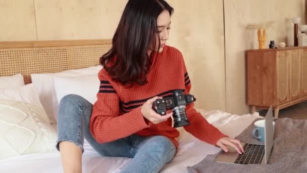 Jeune photographe asiatique en pull travaillant sur ordinateur portable au lit. Femme heureuse révisant les photos prises dans un ordinateur portable. Mode portrait hiver — Video