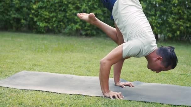 Ung man som övar headstand yoga poserar utanför i trädgården av huset. Kaukasisk manlig yogalärare som tränar och stretchar utomhus i parken medan han gör handstand — Stockvideo