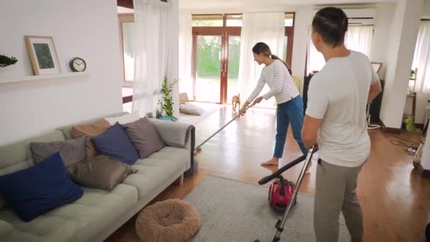 Šťastný mladý pár žena úklid koberec s vysavačem stroj a muž tření podlahu v moderním domě — Stock video