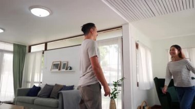 30 'lu yaşlarda Asyalı bir adam evdeki oturma odasında bir kadını tutuyor. Mutlu çift dönüyor ve rahat bir evde heyecan içinde dönüyorlar. Mutlu ilişki hayatı konsepti.