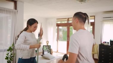 Genç ve mutlu bir çift, dans edip şarkı söylerken elektrikli süpürgeyle temizlik yapıyor ve modern evdeki oturma odasında yerleri paspaslıyor.