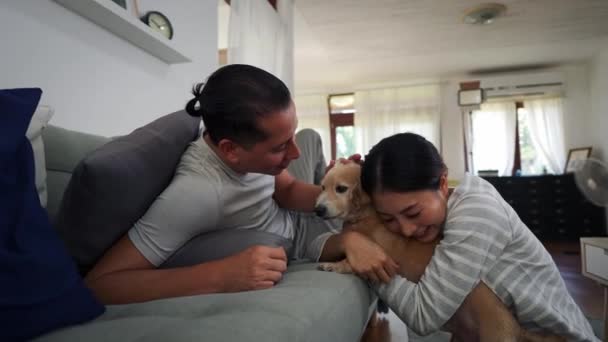 Porträtt av 30-talet ung vuxen man och hustru smeka och klappa en hund husdjur i vardagsrummet hemma. Asiatiska glada och glada par njuta av fritid och leende tillsammans. Hundvänskap koncept — Stockvideo