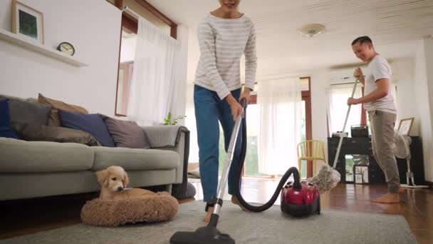 Happy young couple of woman cleaning carpet with vacuum cleaner machine and man mopping the floor at modern home — Stock Video