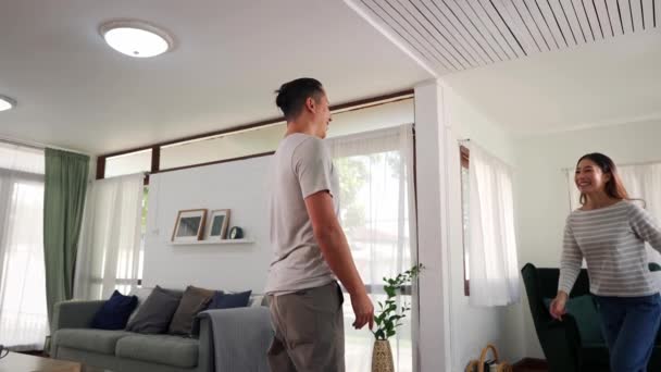 30 éves, fiatal ázsiai férfi, aki otthon tartja a nőt a nappaliban. Boldog pár forog és forog az izgalomtól a hangulatos házban. A boldog kapcsolat fogalma. — Stock videók
