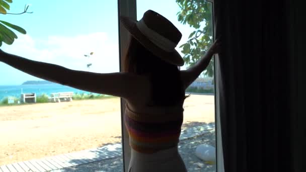 Jovem mulher abrindo as cortinas e vendo através da janela vista mar praia em resort hotel de luxo — Vídeo de Stock