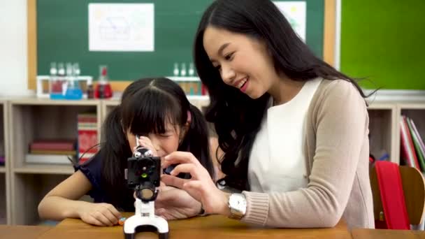 Azjatycki nauczyciel szkolny pomaga uczniom używać mikroskopu — Wideo stockowe