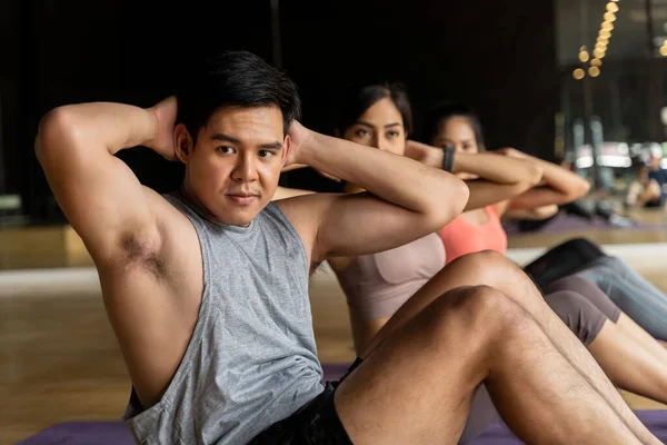 Группа азиатских женщин и мужчин, занимающихся упражнениями на ковриках для йоги в классе аэробики. Молодые спортсмены крутят тело на полу в спортзале. — стоковое фото