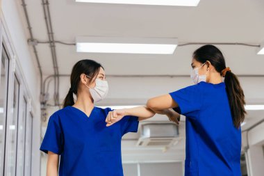 Ameliyat üniforması giyen, yüz maskesi takan genç, güzel Asyalı tıp hemşireleri hastanede dirsek tokuşturuyorlar. Covid19 salgını sırasında işyerindeki profesyonel doktor. Yeni normal karşılama kavramı.