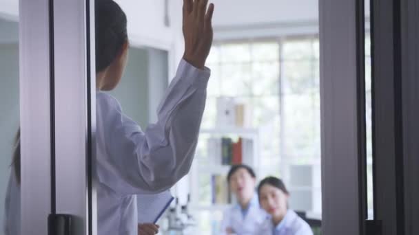 Pandangan belakang terhadap dokter perempuan muda yang memegang papan klip mengarah ke pintu kaca saat sedang bertemu dengan rekan-rekan di ruang konferensi rumah sakit — Stok Video