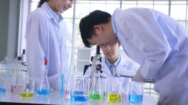 Grupp unga manliga och kvinnliga asiatiska forskare i labcoat som arbetar tillsammans i labb med mikroskop för att studera och utveckla nytt antivirusvaccin — Stockvideo
