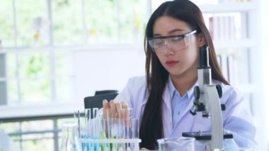 Laboratuvarda test tüpleri ve mikroskop ile tıbbi araştırma yapan, çalışkan ve güzel Asyalı kadın bilim adamı.