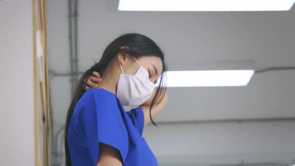 Fáradt és frusztrált fiatal ázsiai női orvos egyenruhás és sebészeti maszkot visel szenved a nyakfájás, miközben dolgozik a kórházban során covid-19 járvány — Stock videók