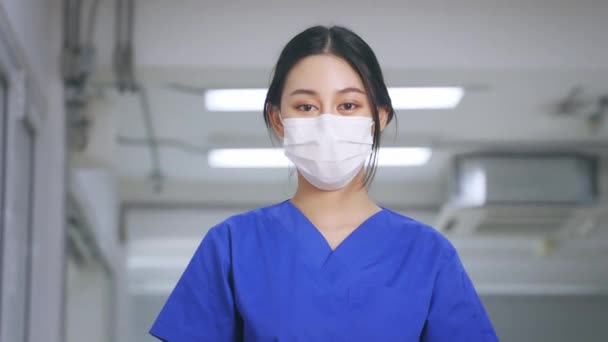 Ung og vakker, selvsikker sykepleier i uniform, med armkryss med ansiktsmaske på, ser mot kameraet med stolthet på å tjene pasienter infisert med kovid-19 – stockvideo