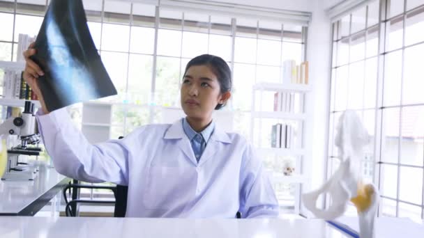Médica asiática sentada em cabine hospitalar lendo e analisando questão nos pulmões de paciente com filme de raios-x em jaleco — Vídeo de Stock