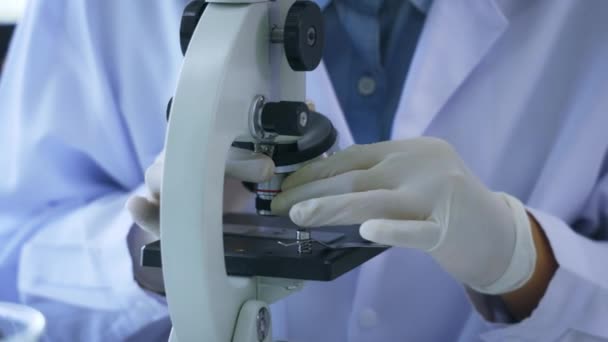 Primo piano dello scienziato che indossa un mantello medico che effettua ricerche in laboratorio mentre vede gli elementi attraverso il microscopio con le attrezzature — Video Stock