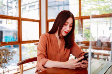 Kafede akıllı telefon kullanan genç bir kadın.