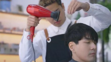 Müşteri üzerinde saç kurutma makinesi kullanan genç kuaför.