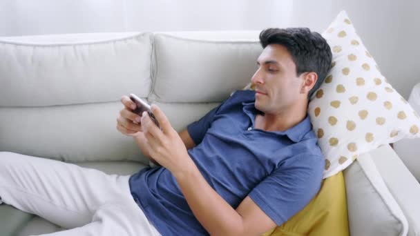 Hombre acostado en el sofá usando un teléfono inteligente — Vídeo de stock