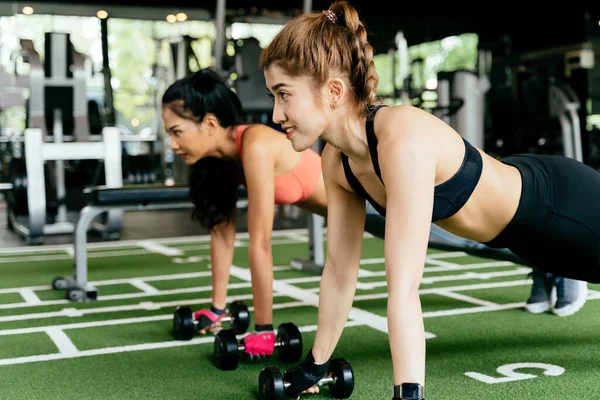 Glückliche junge Sportlerinnen, die mit Freundin Liegestützübungen im Fitnessstudio machen. Gruppe von zwei selbstbewussten Frauen mit gesundem Lebensstil, die gemeinsam auf dem Boden trainieren. — Stockfoto