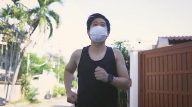 Şehirde maskeli genç bir adam koşuyor. Erkek koşucu sokakta egzersiz yapıyor ve koşuyor.