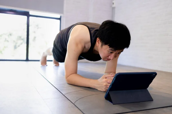 Junger Mann übt zu Hause, während er ein Video-Tutorial auf dem Tablet anschaut. Männliches Fitnesstraining in Innenräumen online — Stockfoto