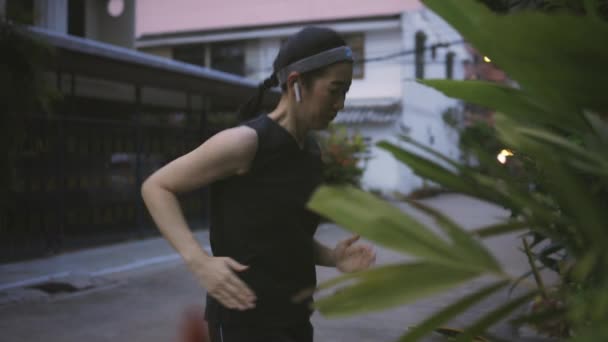 Junge asiatische Läuferinnen der 30er Jahre wärmen sich vor dem Cardio-Training in der Straße der Nachbarschaft in Thailand auf. Verschwitzte Frau in Sportbekleidung und drahtlosem Ohrhörer. — Stockvideo