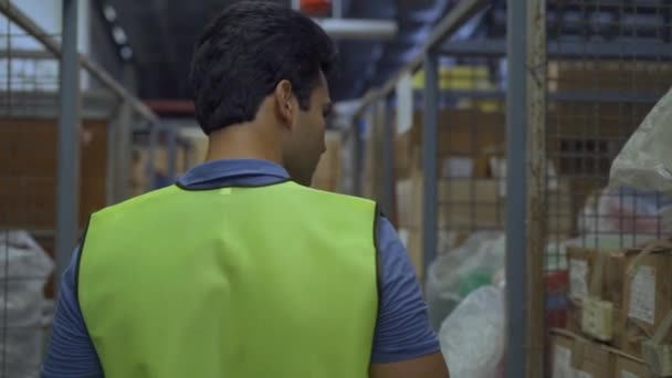 20s Indian distribution shipping depot worker walking and check inventory. Male worker in working uniform at storehouse. Logistics shipment center career concept - Front View — Stock Video