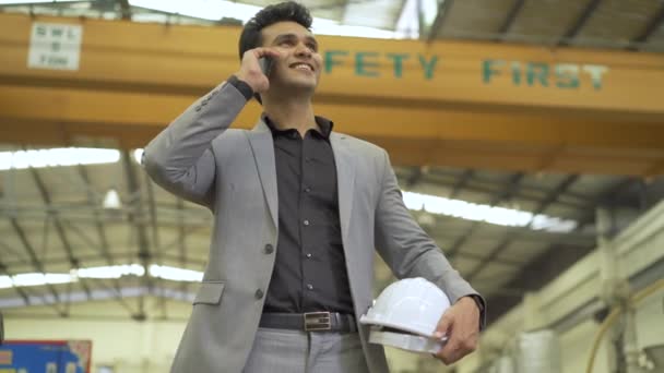 Νεαρός 20άρης Ινδός επιχειρηματίας σε εργοστάσιο της Ασίας με επίσημο κοστούμι που μιλάει στο τηλέφωνο. Επιτυχές επιχειρηματικό εκτελεστικό πορτρέτο στο βιομηχανικό υπόβαθρο — Αρχείο Βίντεο