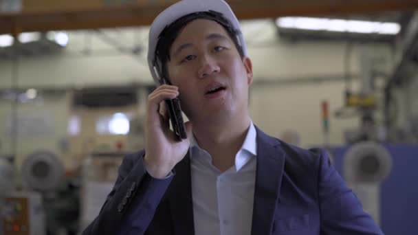 Молодий бізнесмен азіатського заводу в офіційному костюмі і шолом, який розмовляє по мобільному телефону. Конфіденційний адміністратор робить телефонний дзвінок на промисловій фабриці. — стокове відео