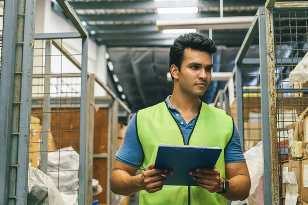 20s Indian distribution shipping depot worker walking and check inventory. Male worker in working uniform at storehouse. Logistics shipment center career concept — Stock Photo, Image