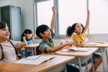 Asyalı ilkokul öğrencisi sınıfta el kaldırdı. Eğitim kurma okulunda ilköğretim çağındaki çeşitli anaokulu öğrencileri. Gönüllü ve katılımcı sınıf konsepti