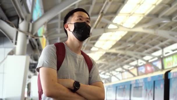 Primer plano de un joven asiático que llevaba una máscara facial quirúrgica negra esperando el tren durante el nuevo brote de neumonía tipo Coronavirus Covid-19 y la crisis de contaminación atmosférica por smog pm 2.5 en la gran ciudad — Vídeos de Stock