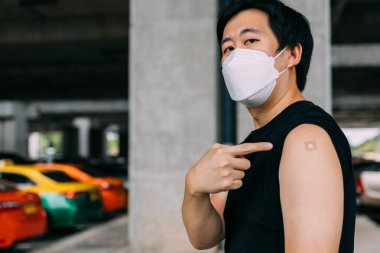 Aşılanmış genç adam Covid-19 aşısı olduktan sonra kollarını yapıştırıcı bandajla sargılıyor.