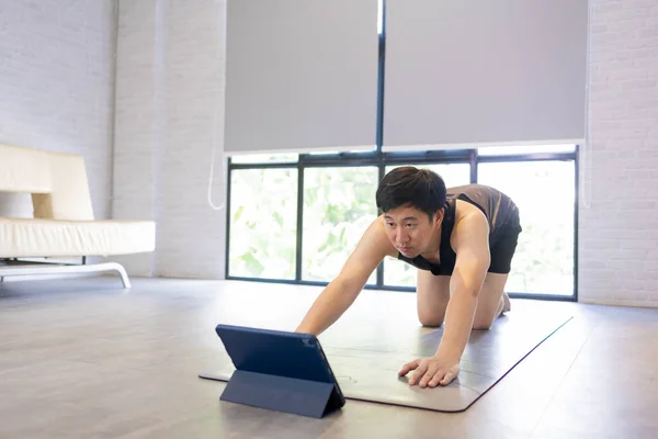 Jongeman die thuis traint terwijl hij een video-tutorial op tablet bekijkt. Mannelijke fitness man training binnen online — Stockfoto