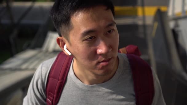 Joven asiático escuchando música con auriculares inalámbricos sobre la marcha en tren en la estación — Vídeo de stock