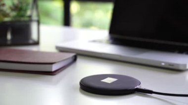 Akıllı telefon, masadaki dizüstü bilgisayar, gözlük ve defterle birlikte kablosuz şarjla şarj ediliyor.