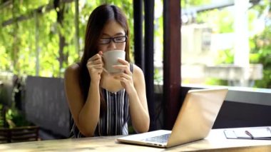 Gözlüklü, gülümseyen ve dizüstü bilgisayarını karıştıran Asyalı bir kız öğrencinin yaz günü terasta oturup ders çalışması.