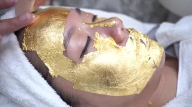 Young woman getting 24 karat gold facial treatment at the beauty clinic