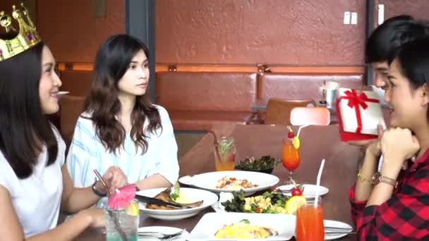 若いアジアのカップルは現在のギフトボックスと友人を与えます近くのレストランで手を拍手 — ストック動画