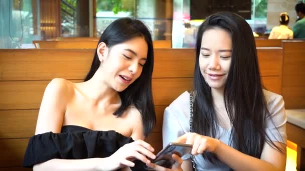 Two Asian female friends using mobile phone and laughing together. Women enjoying at restaurant — Vídeo de stock