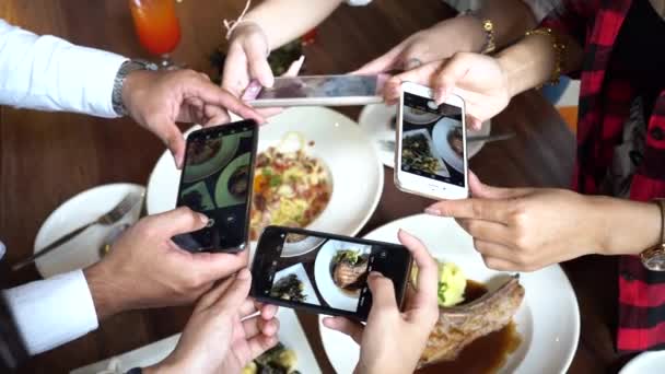 Four young people using mobile phone and taking photos of spaghetti and food at restaurant — стоковое видео