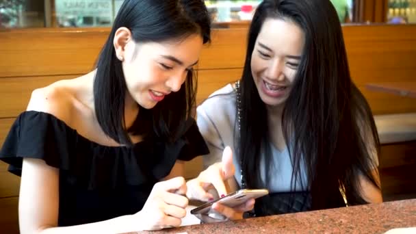 Two Asian female friends using mobile phone and laughing together. Women enjoying at restaurant — Vídeo de Stock