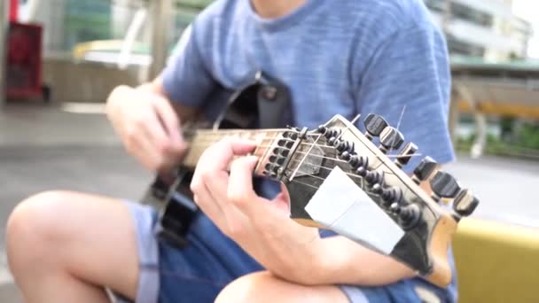 Street musician strumming guitar on the street outdoors while passerby walking by — Stockvideo
