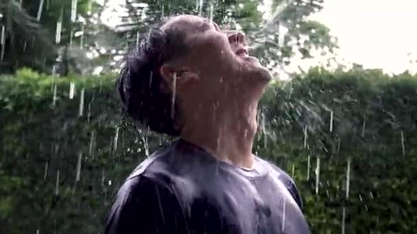 Young Asian man standing out in middle of the rain and looking up at the sky full of emotions — Vídeo de stock