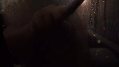 Person drawing smiley face with vapor steam on glass window