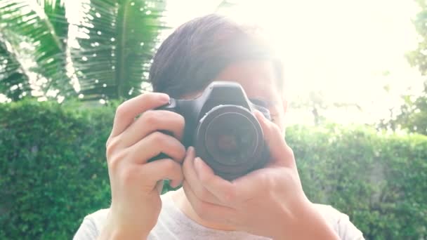 Young male photographer taking photos during sunset with back-lighting lens flare from behind — Stockvideo