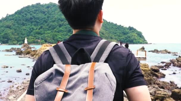 Follow shot of Rear view portrait of a young Asian man walking at beach with bag — Stockvideo